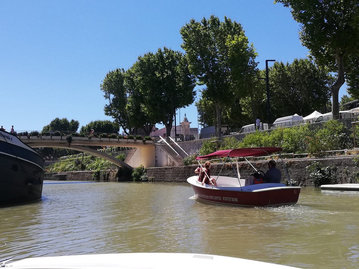 deux personnes naviguant sur le canal de la robine à narbonne à bord d'un bateau électrique sans permis rouge